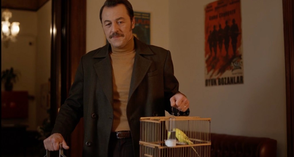 Kafes içindeki kuşla birlikte duran erkek karakter; Parçalı Yıllar filminden sembolik bir an.
