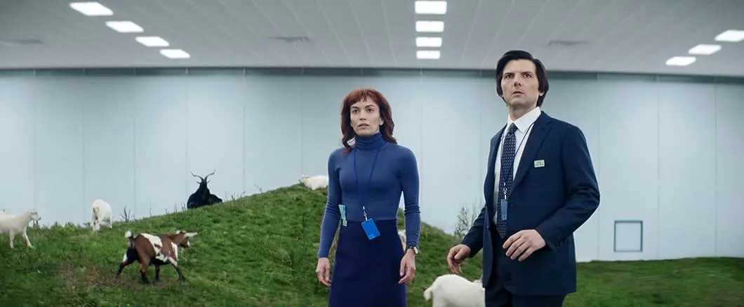 Severance dizisinde Lumon ofisinin yeşil zeminli koridorunda yürüyen iki çalışan, steril ve yapay ofis atmosferi