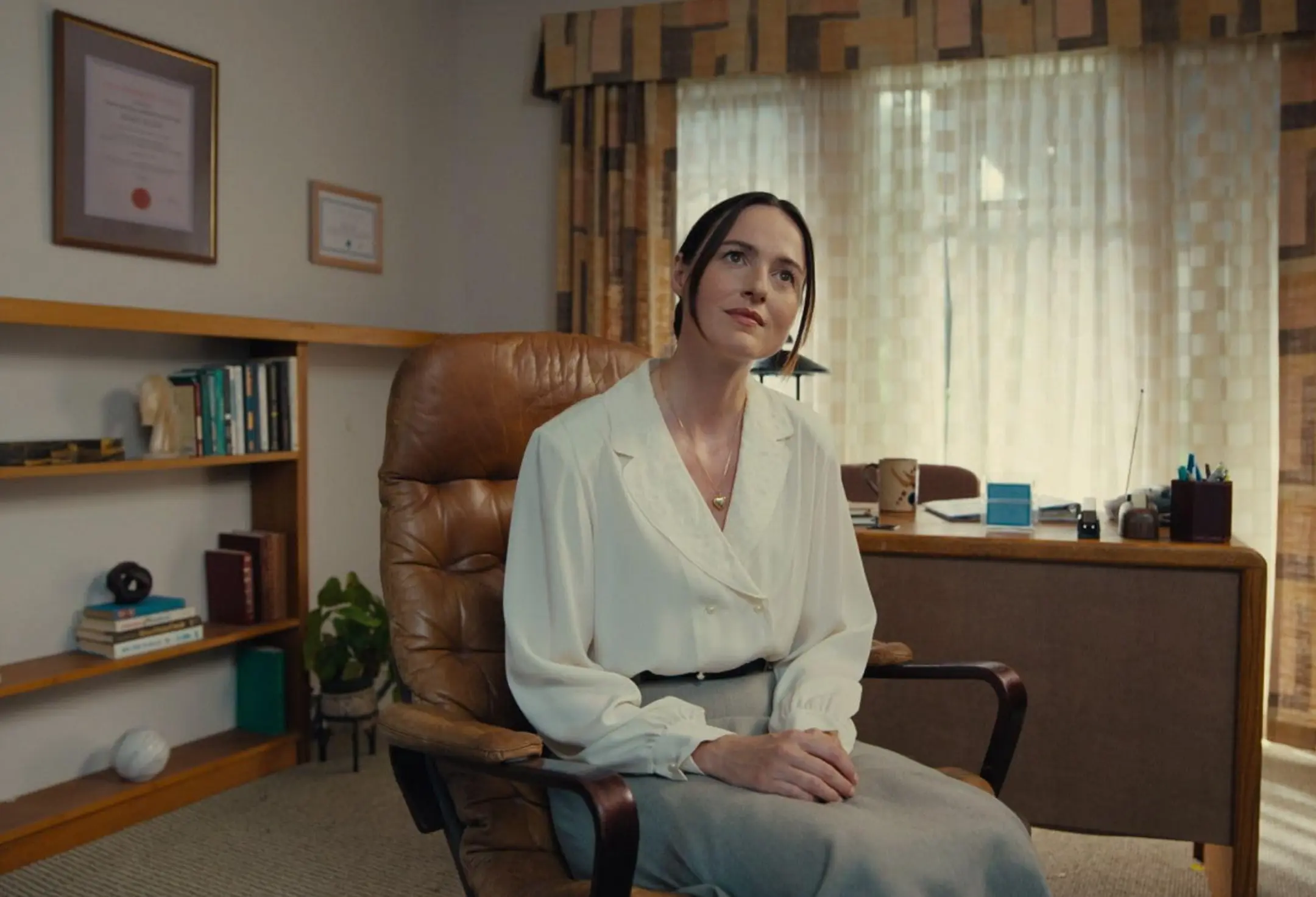 Renate Reinsve Backrooms 2026 filminden odada beyaz gömleği masaya oturuyor.