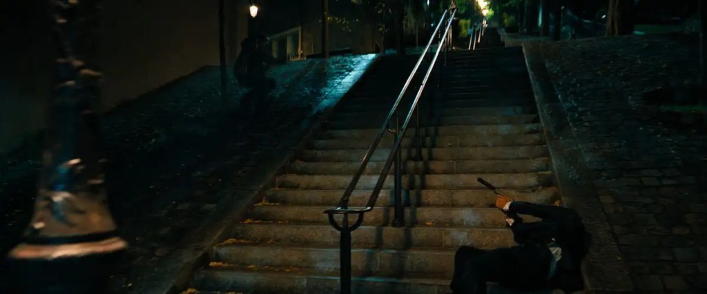 John Wick, Sacré-Cœur merdivenlerindeki mücadelesi sırasında basamaklardan aşağı düşüyor.